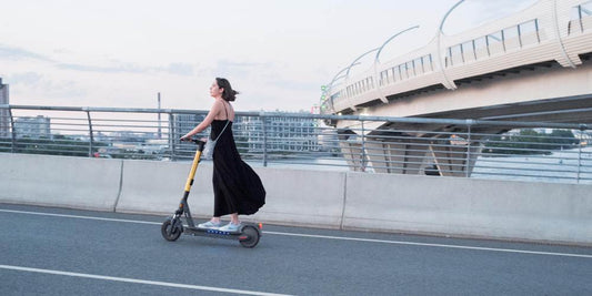 Dziewczyna w czarnej sukience jadąca na hulajnodze elektrycznej po ulicy.