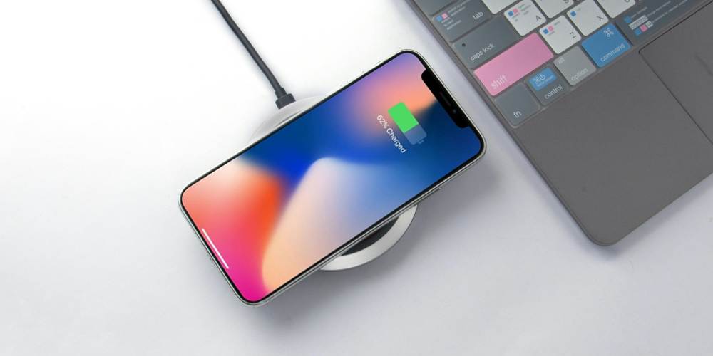 Ładowanie bezprzewodowe smartfona. Obok na zdjęciu kawałek laptopa.
